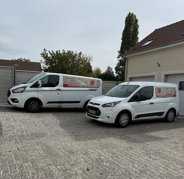 Deux camionnettes de service blanches garées devant un bâtiment beige avec un toit marron à Longnes dans les Yvelines 78