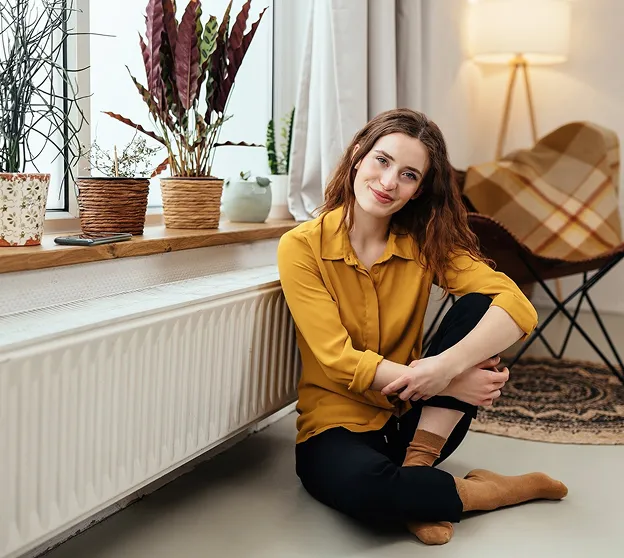 Jeune femme assise sur le sol près d'une fenêtre avec des plantes d'intérieur.