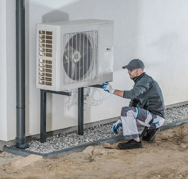 Technicien en casquette et lunettes de soleil travaillant sur une pompe à chaleur extérieure à Longnes dans les Yvelines 78