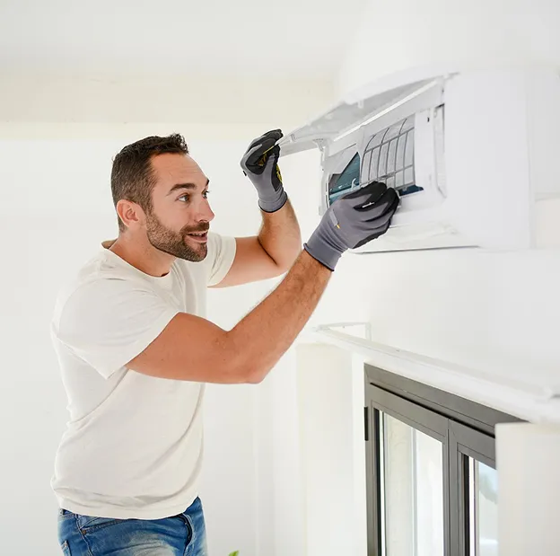 Homme barbu ganté nettoyant le filtre d'un climatiseur mural blanc à Longnes dans les Yvelines 78