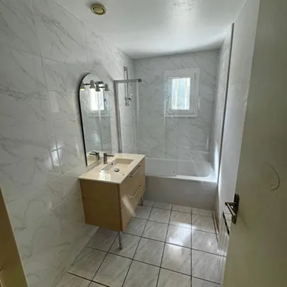 Salle de bain moderne carrelée avec lavabo, miroir, baignoire-douche et fenêtre.