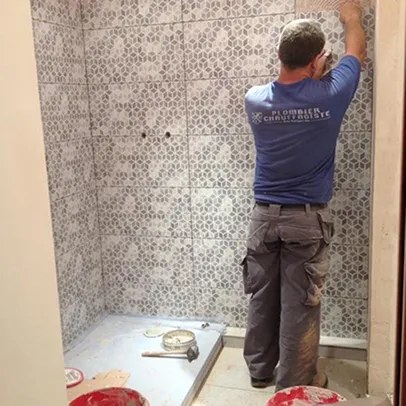 Homme carrelant un mur de douche avec des carreaux à motifs gris et blancs.