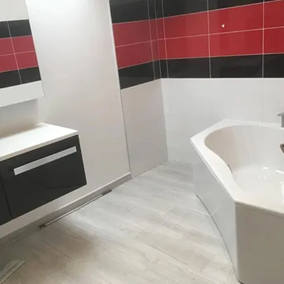 Salle de bain moderne avec carrelage rouge/noir, lavabo suspendu, baignoire blanche et sol clair.